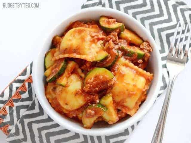 A bowl of zucchini sausage ravioli with sauce and a fork.