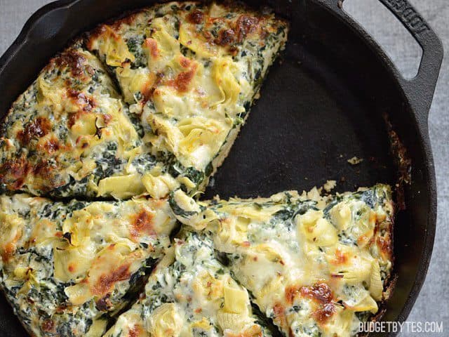 A close-up of creamy spinach and artichoke pizza slice.