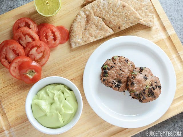 Two Mini Black Bean Turkey Burgers on a plate with pita and toppings on the side