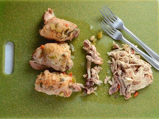 Chicken thighs on the cutting board with forks, meat pulled from bones