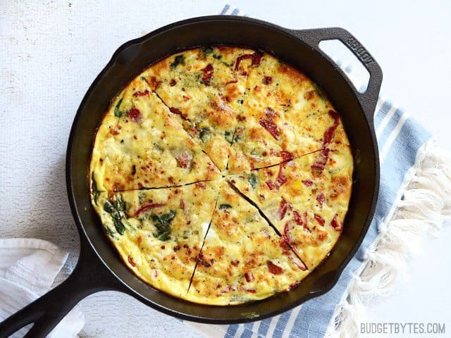 A frittata with roasted red peppers and feta on a cast iron pan.