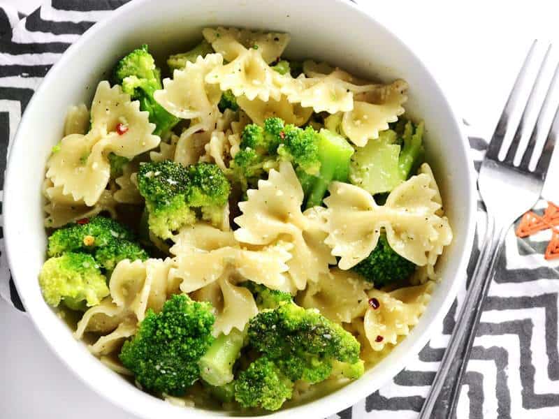 Close up overhead view of a bowl full of bowties and broccoli, on a zig zag napkin