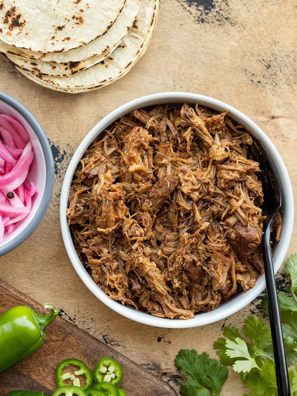 Overhead view of a bowl full of chili rubbed pulled pork with taco fixings on the sides