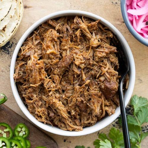 Overhead view of a bowl full of chili rubbed pulled pork with taco fixings on the sides