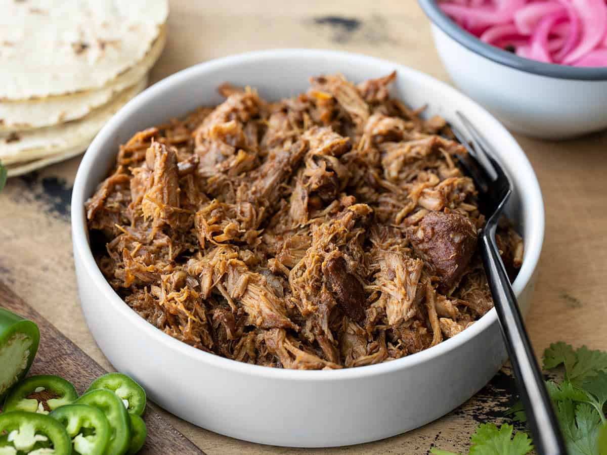 Front view of a bowl full of chili rubbed pulled pork with taco fixings in the back