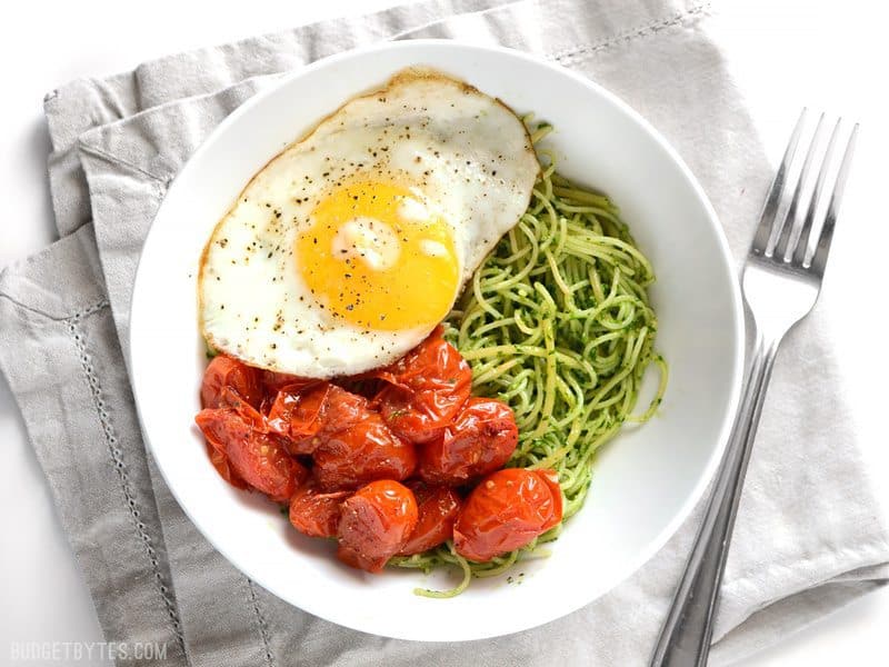 Overhead view of a bowl full of parsley pesto pasta with blistered tomatoes and a fried egg