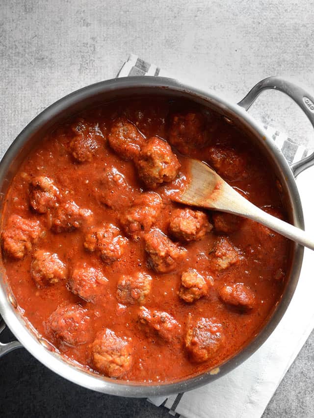 Overhead view of meatballs in sauce in the skillet with a wooden spoon