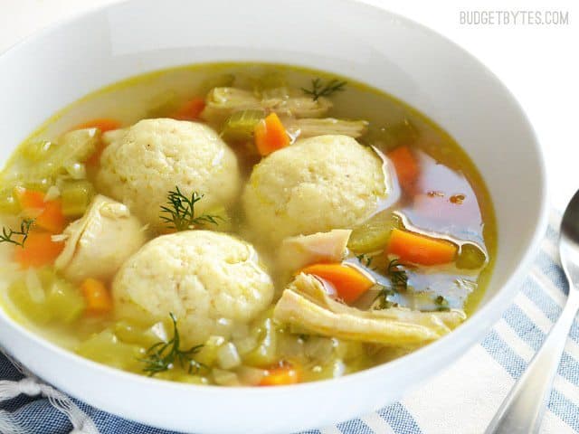 A close-up of matzo ball soup garnished with herbs.