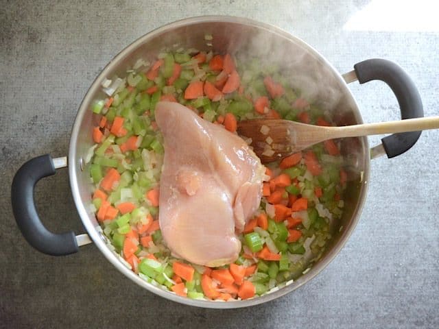 Chopped softened veggies and chicken breast in pot cooking 