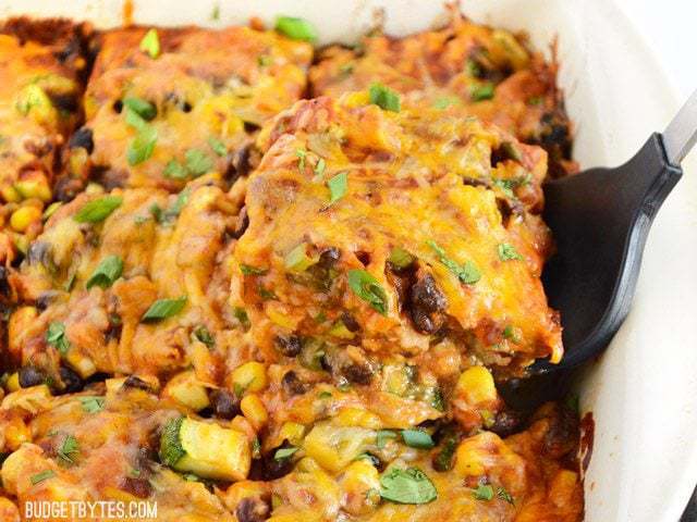 Side view of a spatula lifting a square of Vegetable Enchilada Casserole out of the casserole dish