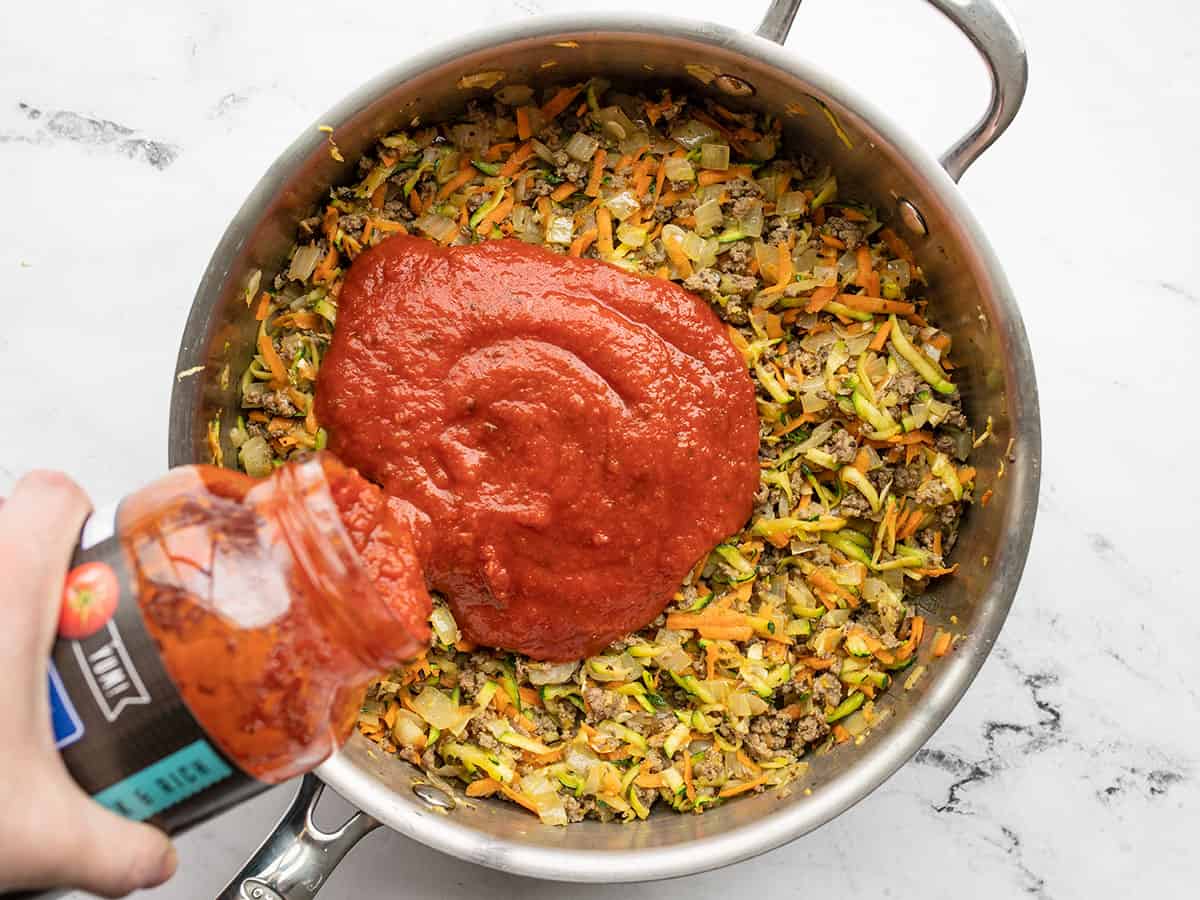 Pasta sauce being poured into the skillet with the meat and vegetables