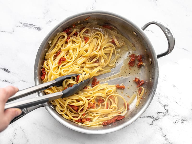 Cooked pasta in the skillet, tongs pulling the pasta aside to show the sauce in the bottom of the skillet