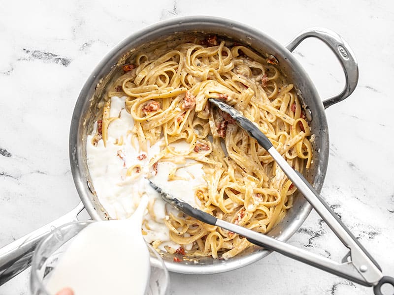 Milk being poured into the skillet full of pasta