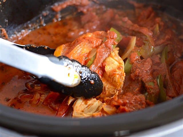 Tongs picking up a piece of chicken in the slow cooker