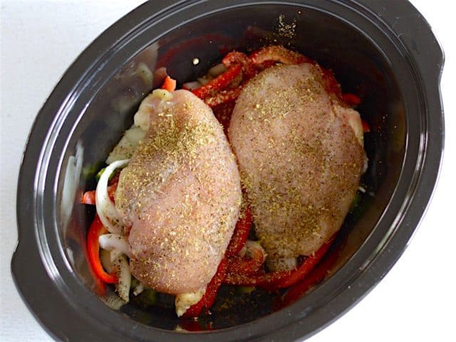 Raw Chicken and Herbs on the peppers and onions in slow cooker