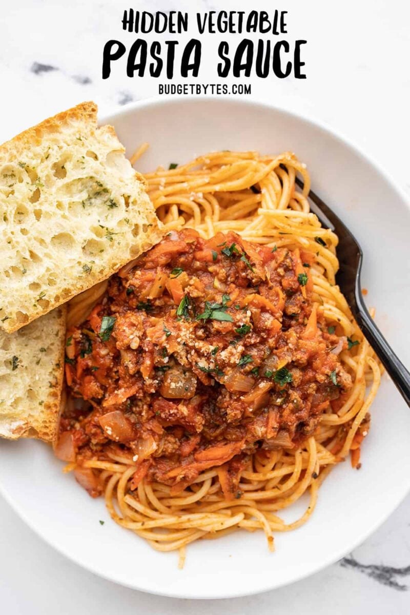 Overhead view of a bowl full of pasta with garlic bread, title text at the top