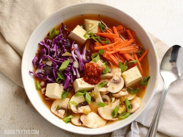 A bowl of hot and sour vegetable soup with herbs with a spoon.