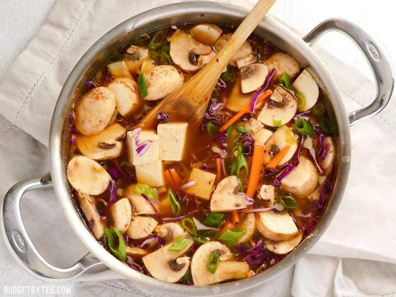 A soup pot full of hot and sour soup with cubed tofu and vegetables, a wooden spoon in the center.