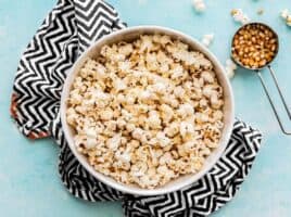 One large bowl of popcorn with a measuring cup of popcorn kernels on the side