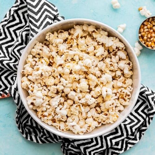 One large bowl of popcorn with a measuring cup of popcorn kernels on the side