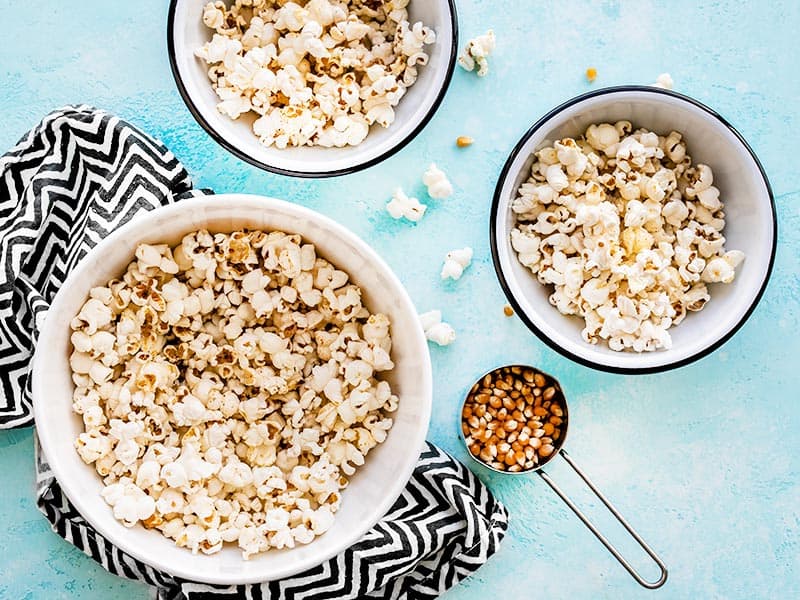 A big bowl of popcorn with two smaller portioned bowls on the side, with a measuring cup of unpopped kernels next to the bowls