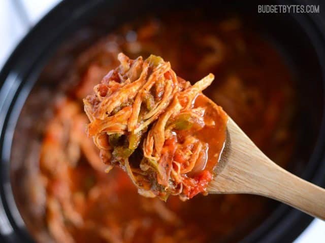 Close up of Italian Chicken and Peppers on a wooden spoon with the slow cooker in the background