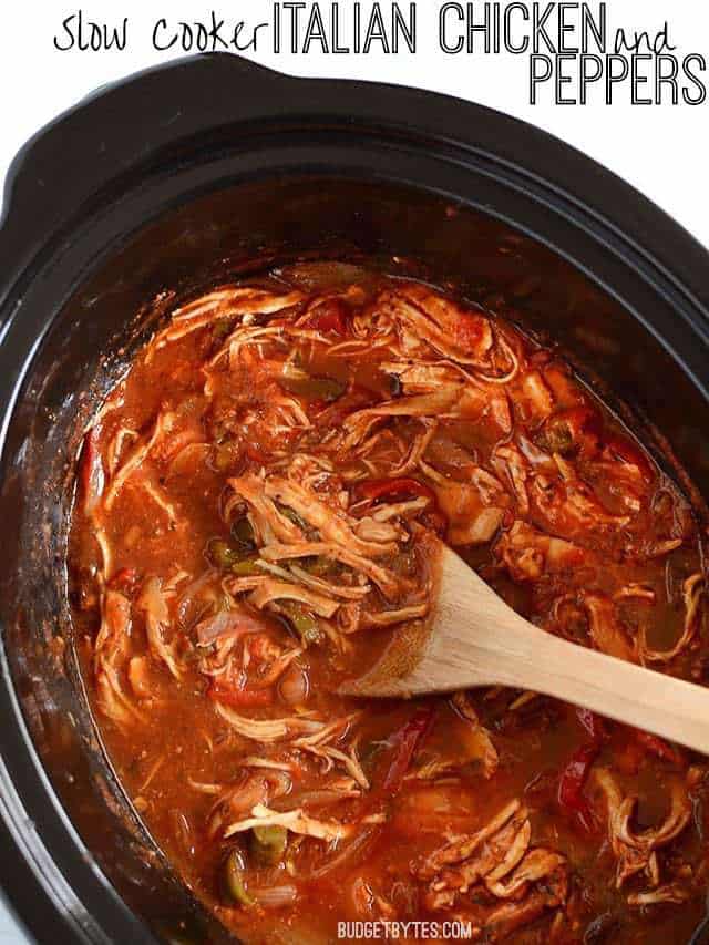 Overhead view of a slow cooker containing Italian Chicken and Peppers, a wooden spoon in the middle