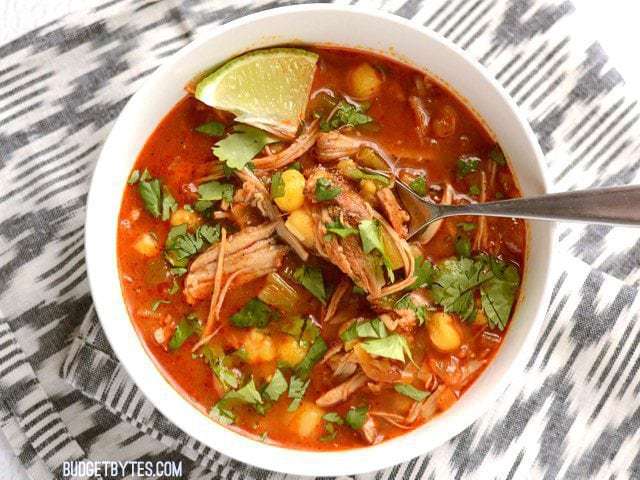 A bowl of posole garnished with lime and cilantro.