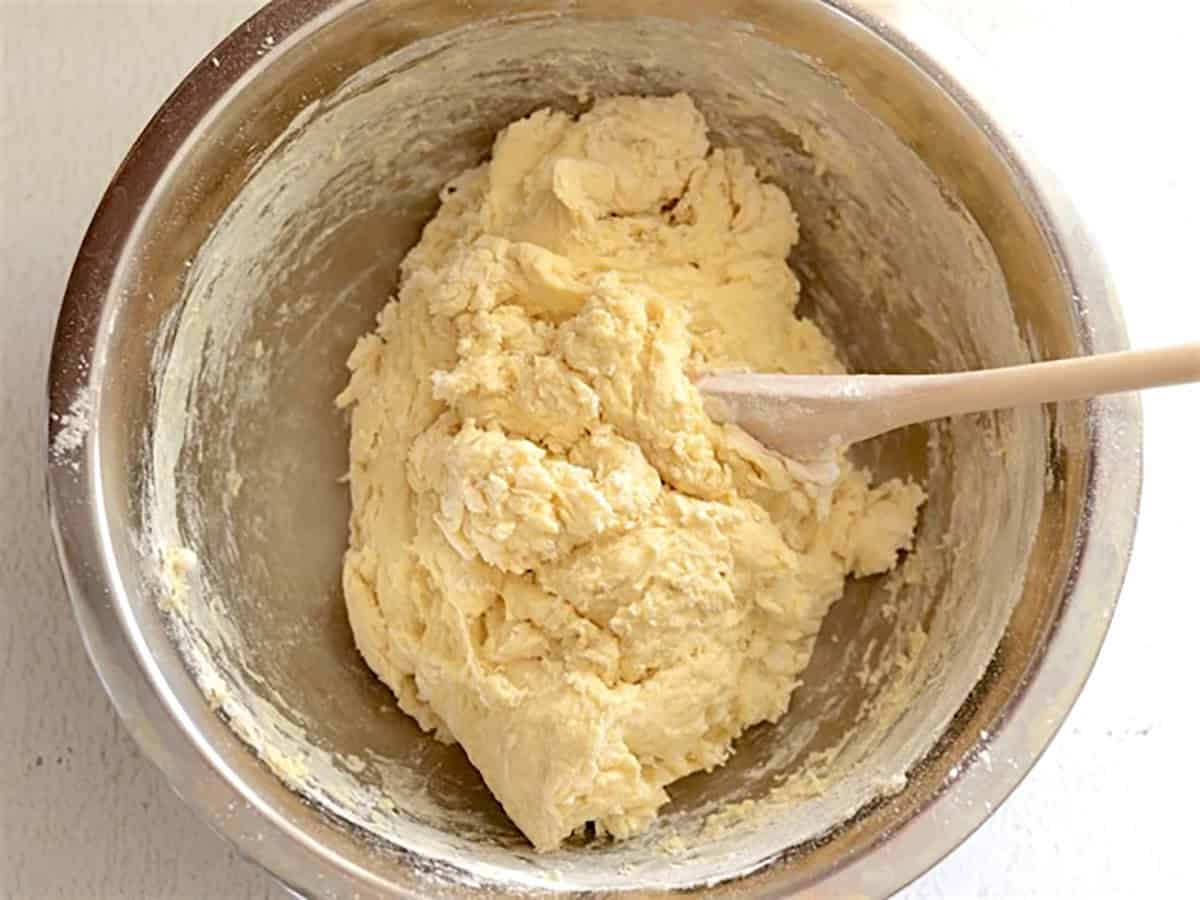 Mixed naan dough in a metal bowl with a wooden spoon.