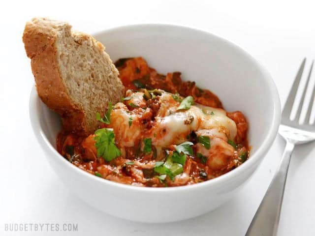 A bowl full of Cheesy Gnocchi with a piece of wheat bread stuck in the side