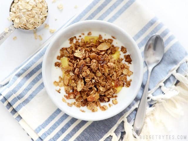 Overhead view of a bowl full of Gingersnap Granola and yogurt, a measuring cup with dry oats on the side