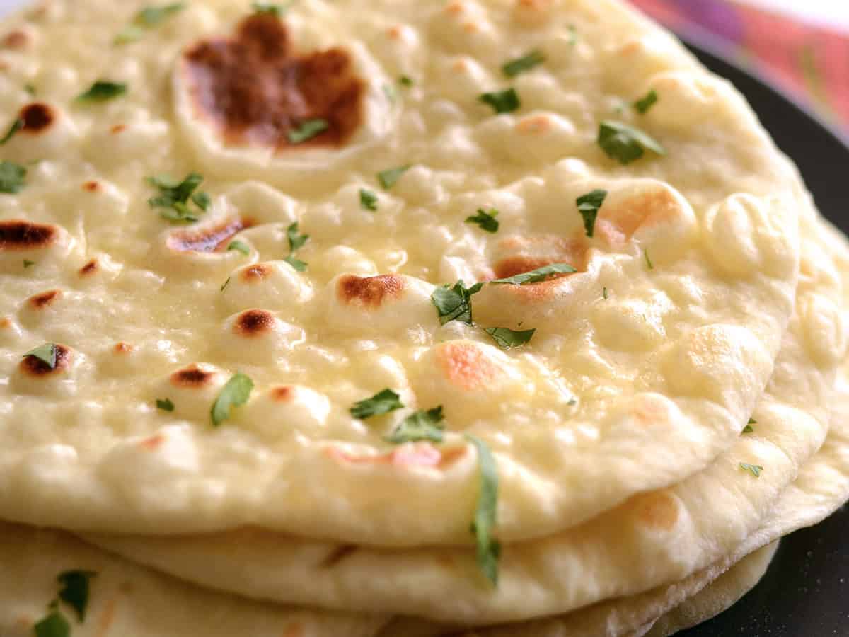 Close up side view of a stack of fresh naan garnished with parsley.