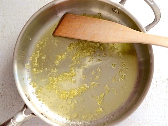 Sautéed Garlic in a skillet with a wooden spatula