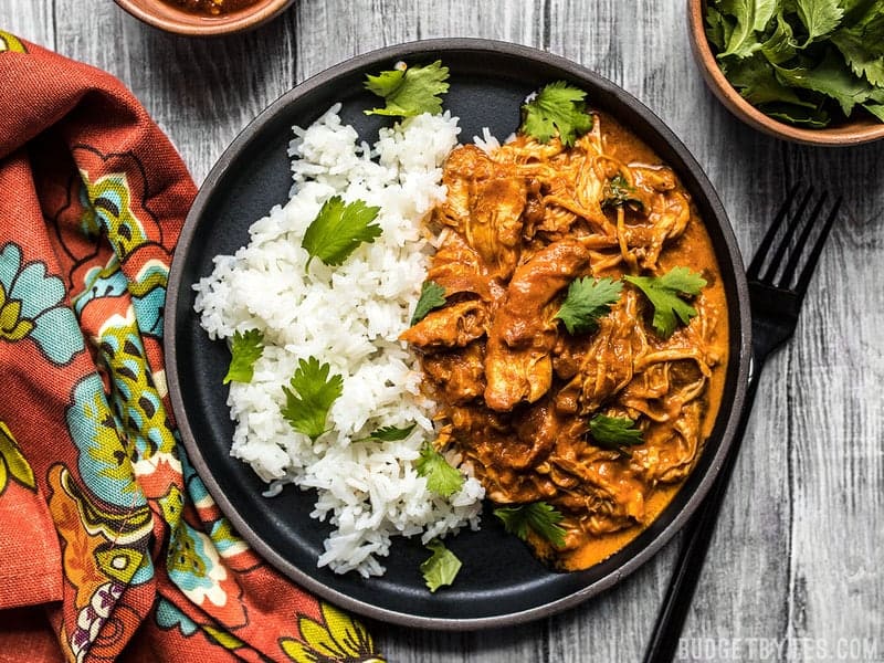 A plate full of slow cooker chicken tikka masala served with rice and cilantro, a colorful napkin on the side. 