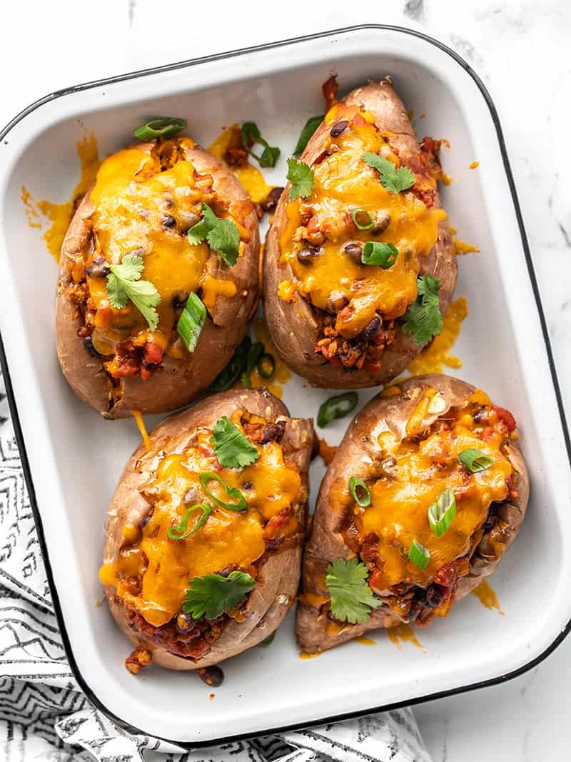 Four turkey chili smothered sweet potatoes in a small white baking dish.