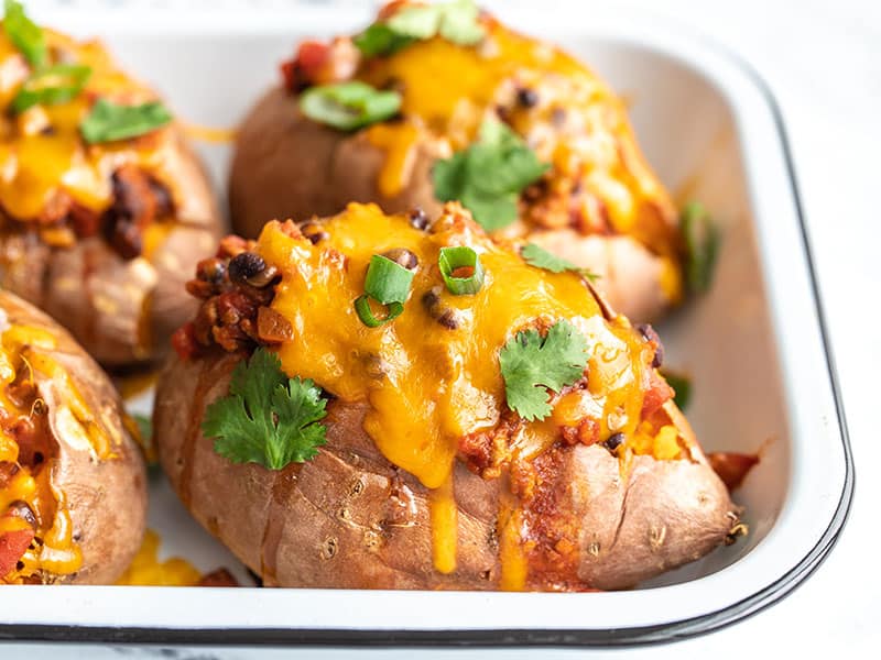 Side view of turkey chili smothered sweet potatoes in a baking dish, topped with green onion and cilantro