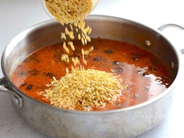 Uncooked orzo being poured into the skillet.