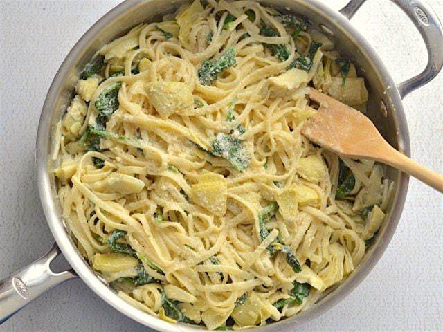 Parmesan cheese being added to a dish of spinach artichoke pasta.