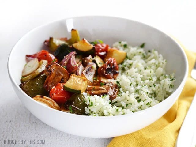 Broiled Balsamic Vegetables served over lemon parsley rice, in a bowl, sitting on a yellow napkin. Side view.