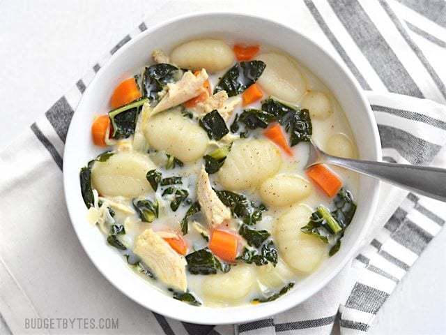 Overhead view of a bowl of creamy chicken gnocchi soup, a spoon in the center