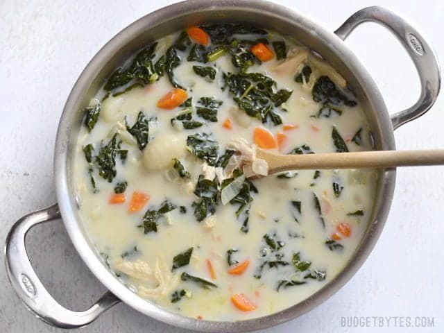 Finished chicken gnocchi soup with kale in the soup pot, a wooden spoon in the center