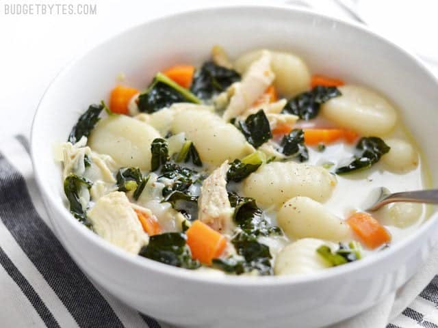 Side view of a bowl of creamy chicken gnocchi soup with kale, a spoon in the center