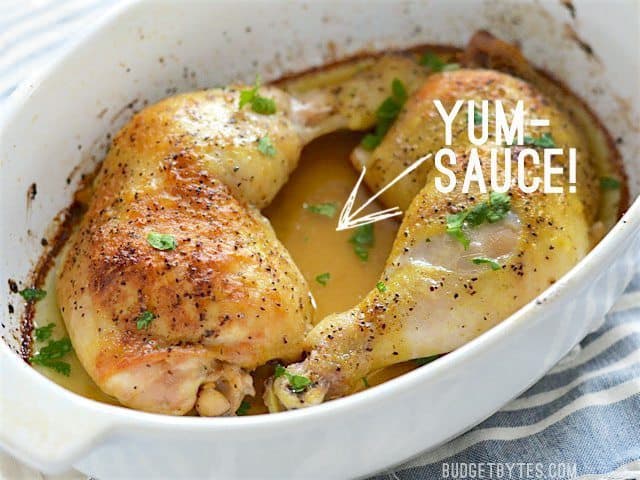 Roasted chicken legs in the casserole dish, garnished with parsley, an arrow pointing at the drippings