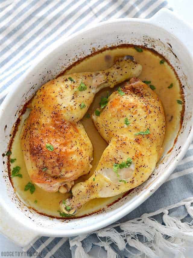 Oven Roasted Chicken Legs in a white casserole dish with baking juices surrounding.