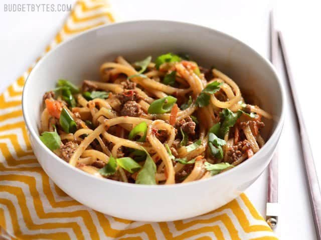 Side view of a bowl full of beef stir fry noodles with chopsticks on the side