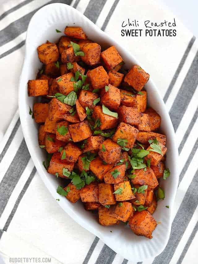 Chili Roasted Sweet Potatoes are an easy and flavorful side dish for any southwest inspired meal. Perfect for busy weeknights and meal prep! BudgetBytes.com An oval white ceramic serving dish full of Chili Roasted Sweet Potatoes garnished with cilantro