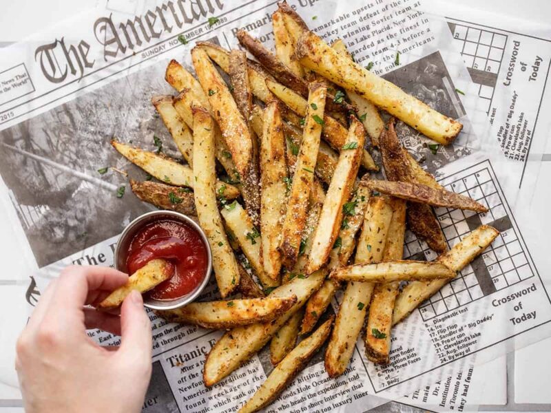 a hand dipping a fry into a cup of ketchup next to a pile of fries