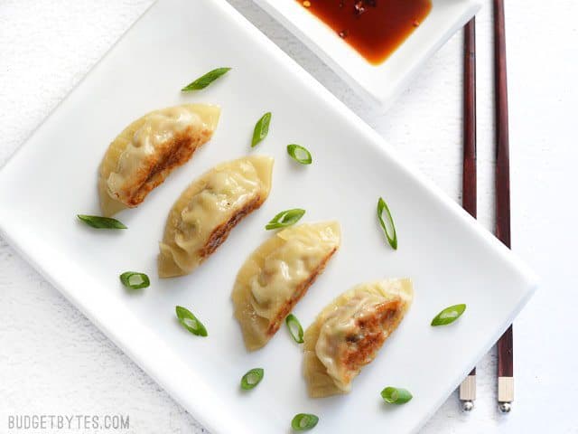 Four Pork Gyoza on a plate, sprinkled with green onion, next to a dish of soy sauce.