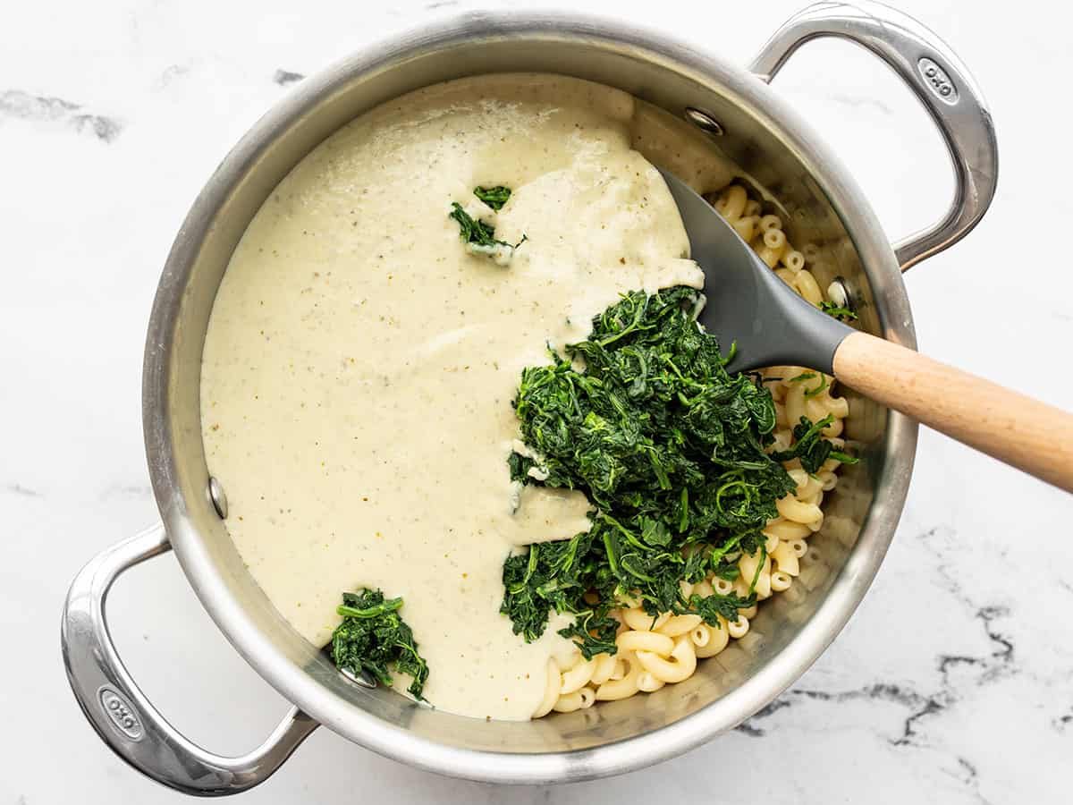 Creamy pesto sauce and spinach added to the pot with the cooked macaroni