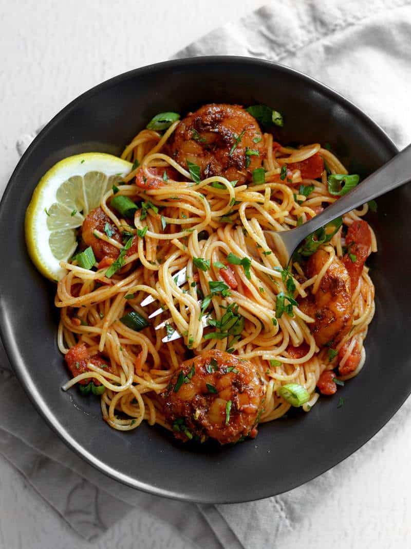 A bowl of Blackened Shrimp Pasta with some wound around a fork and lemon slices on the side